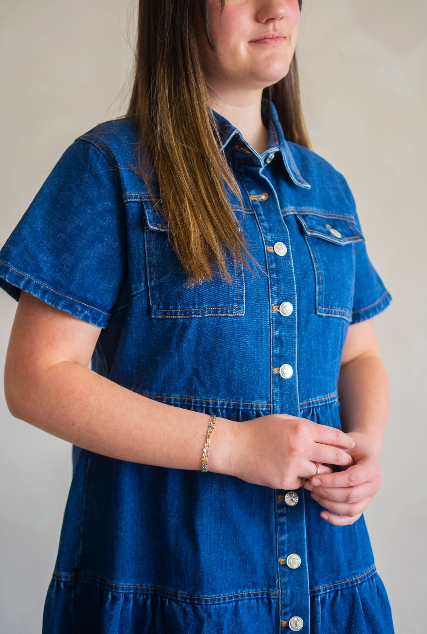 Angled look at the Cassidy denim dress featuring double front pockets, collared neckline, and front buttons.
