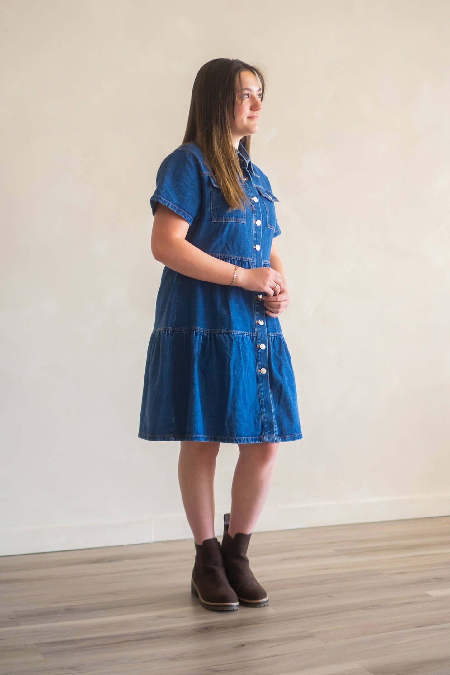 Woman looking off to the right wearing knee length dark wash denim dress.