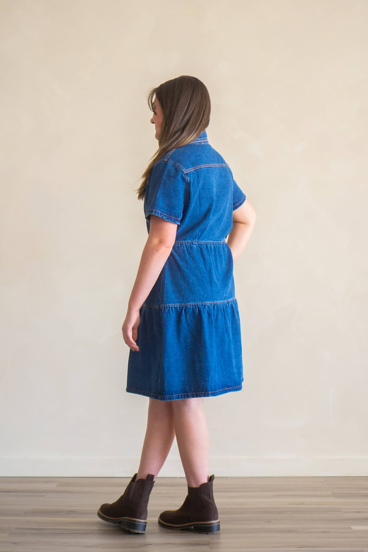 Woman facing away from camera wearing dark wash tiered denim dress in knee-length fit.
