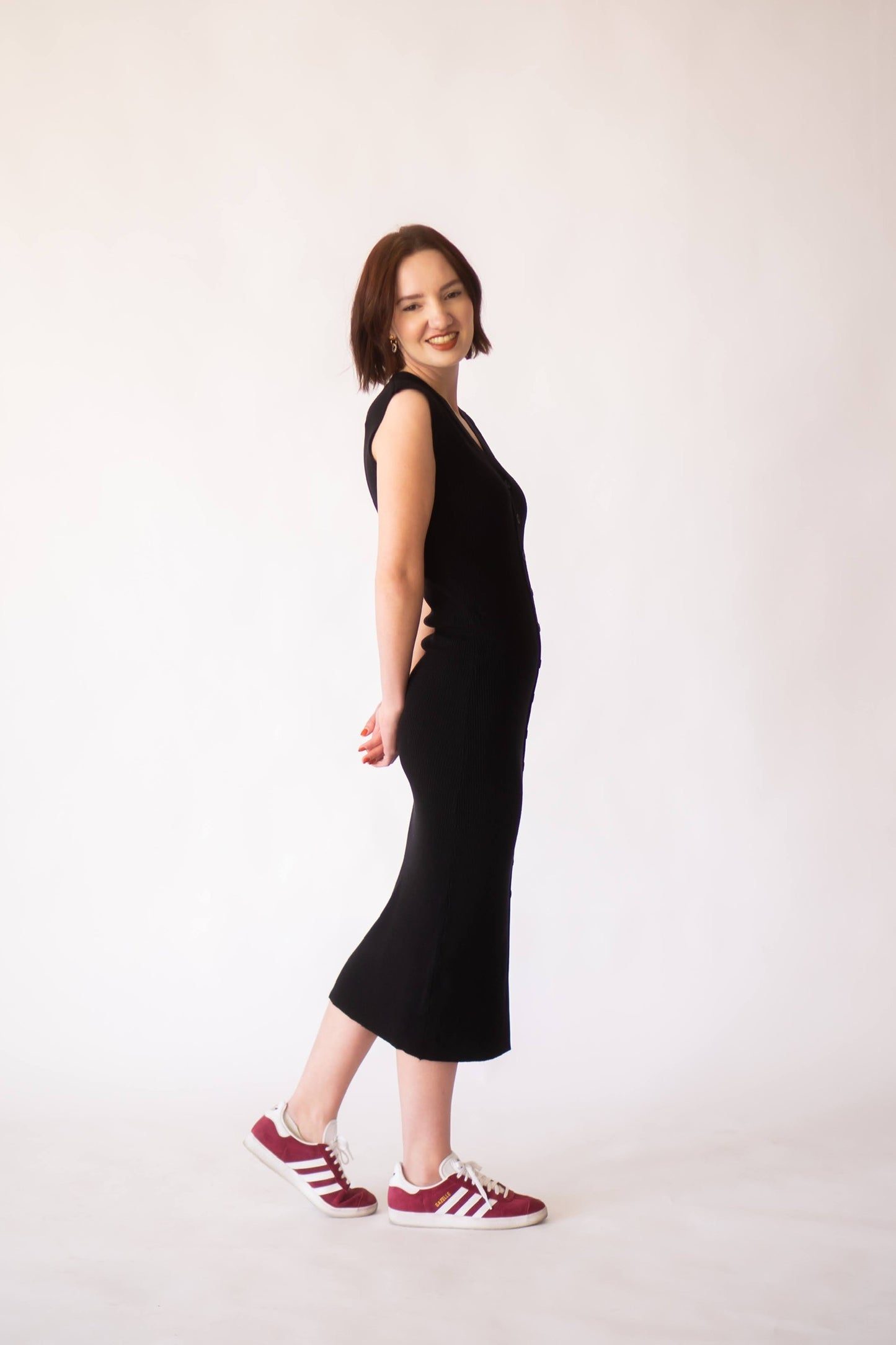 Woman wearing black knit midi dress with buttons smiling at camera.