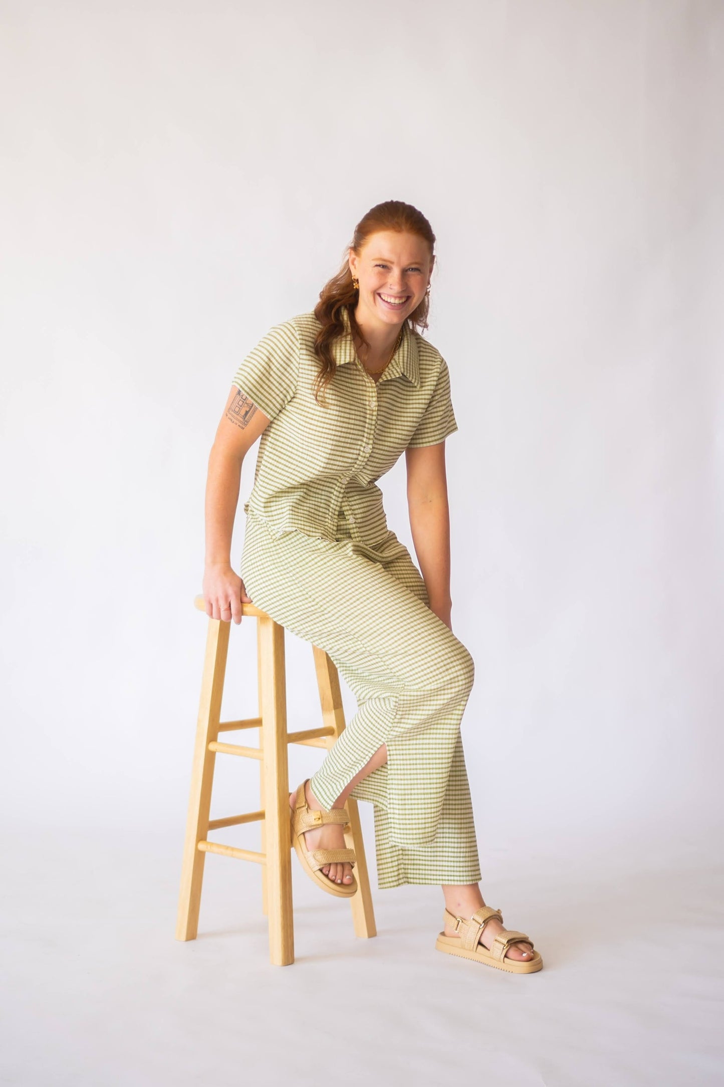 Woman sitting on stool wears green stripe button up top with matching wide leg bottoms