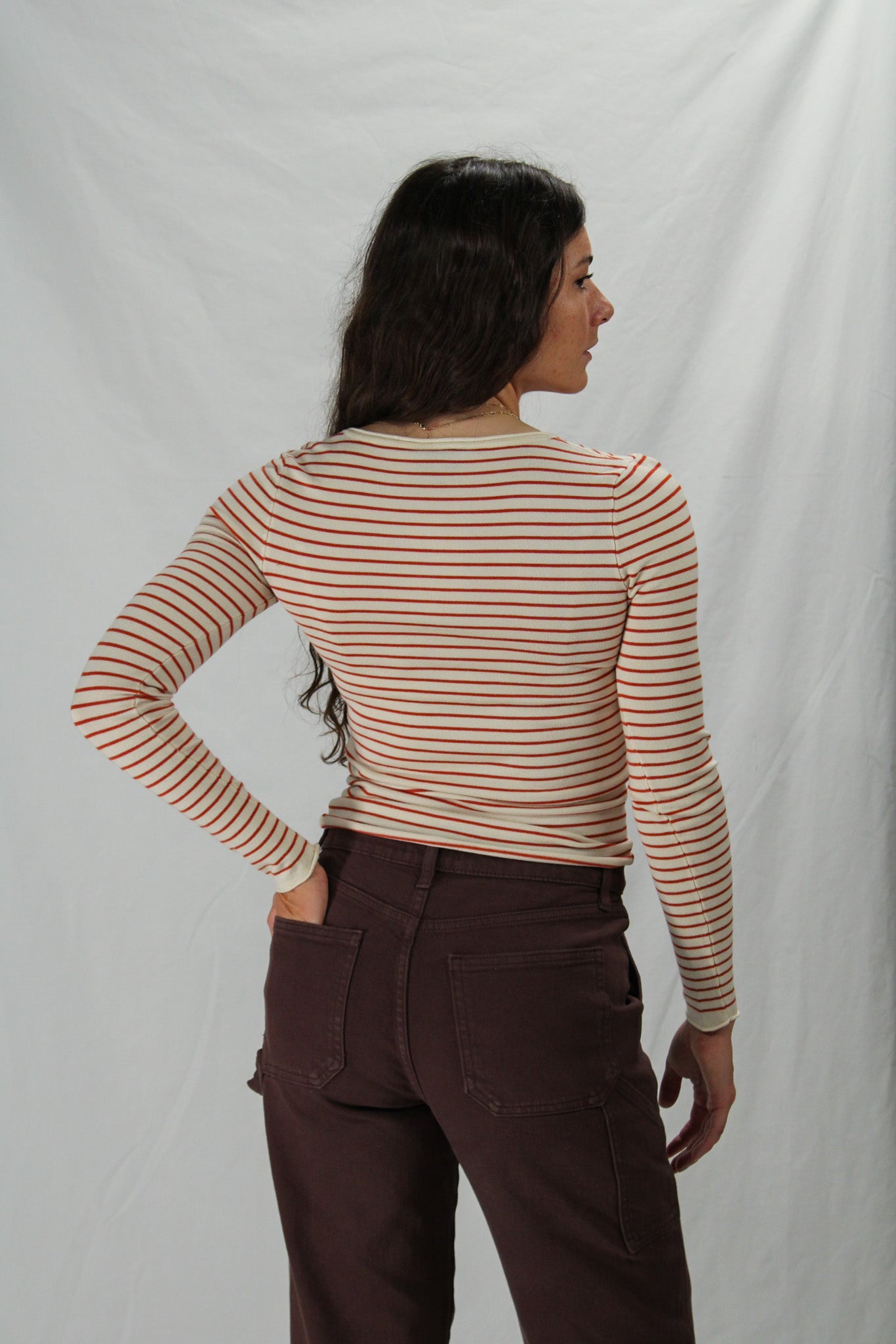 Woman wearing a cream & rust striped long-sleeve top and brown pants against a white background