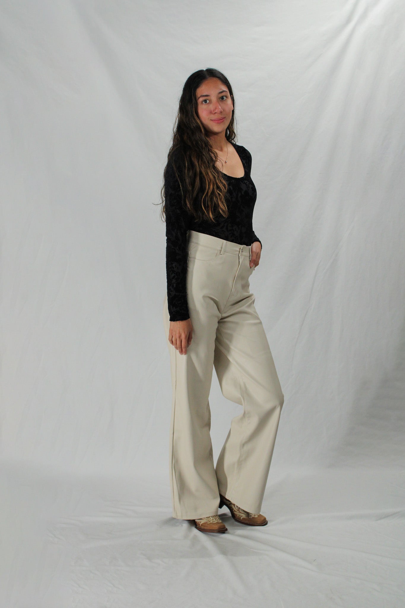 Woman wearing cream leather pants with cowboy boots and a black scoop neck top
