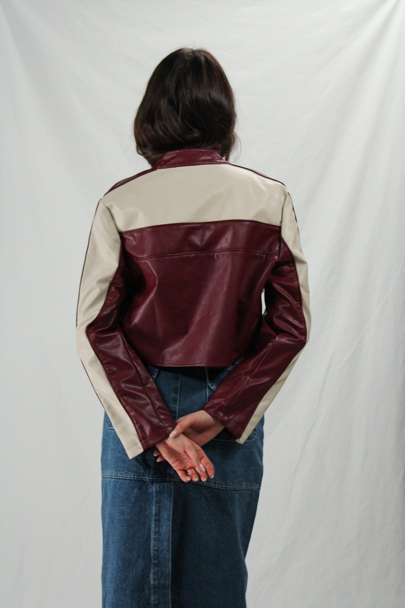 Woman wearing a two-tone leather jacket with burgundy and beige sections on a plain background
