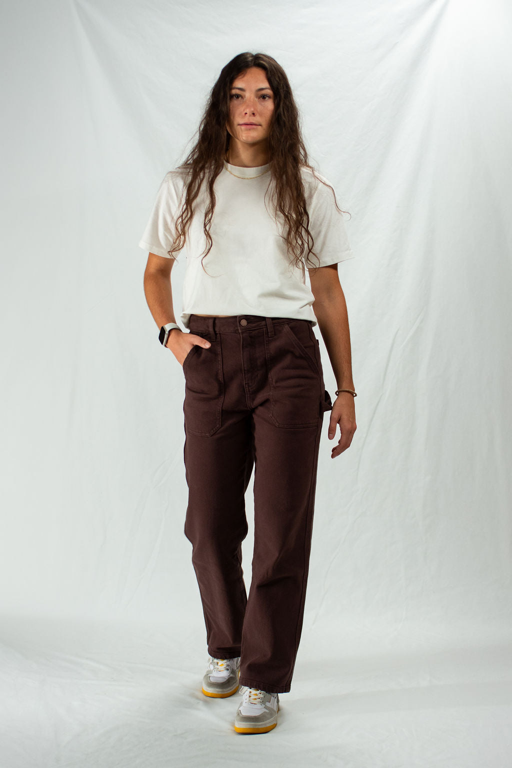 Woman wearing a white t-shirt and brown carpenter pants on a plain background