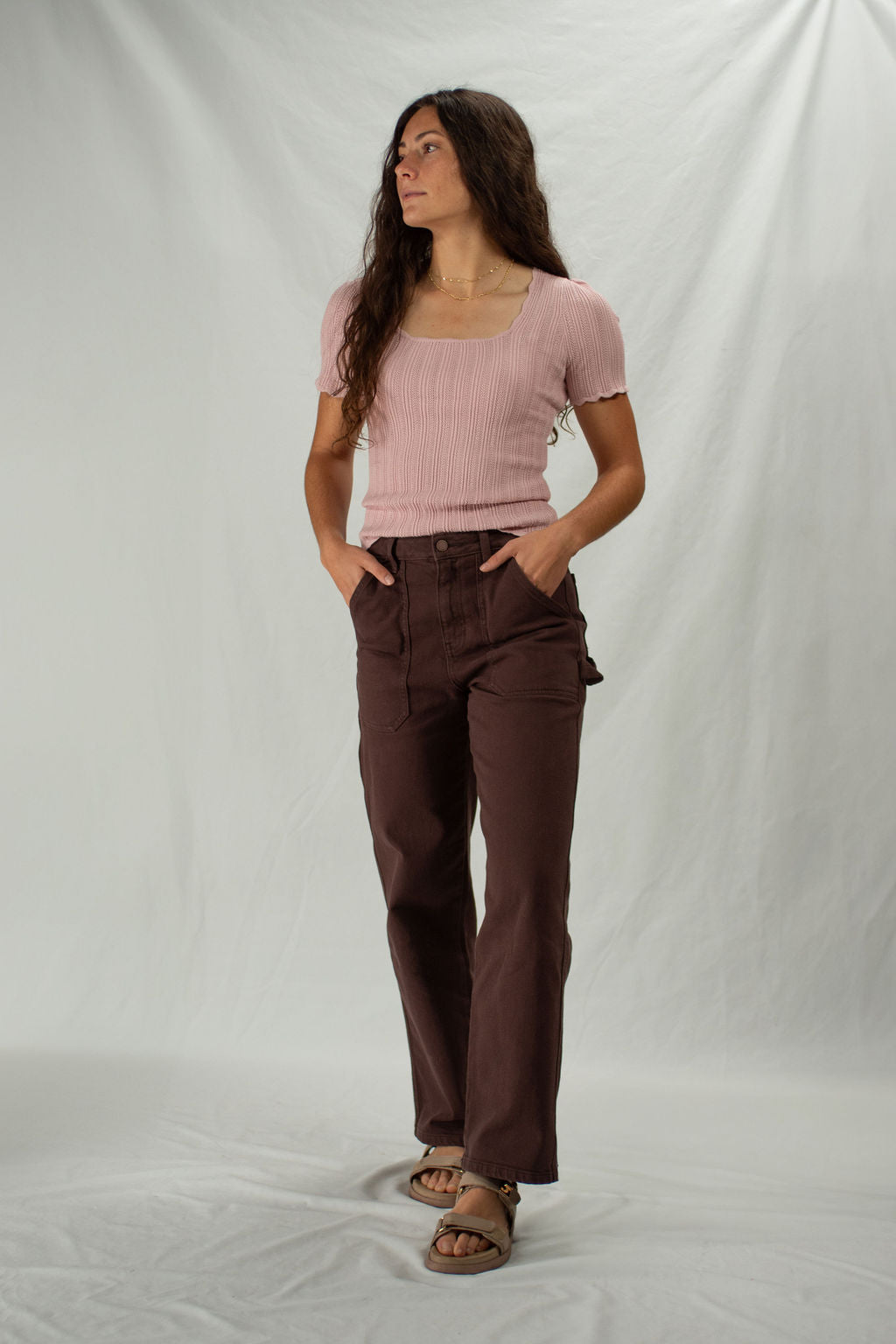 Woman wearing a pink top and brown cargo pants against a white background