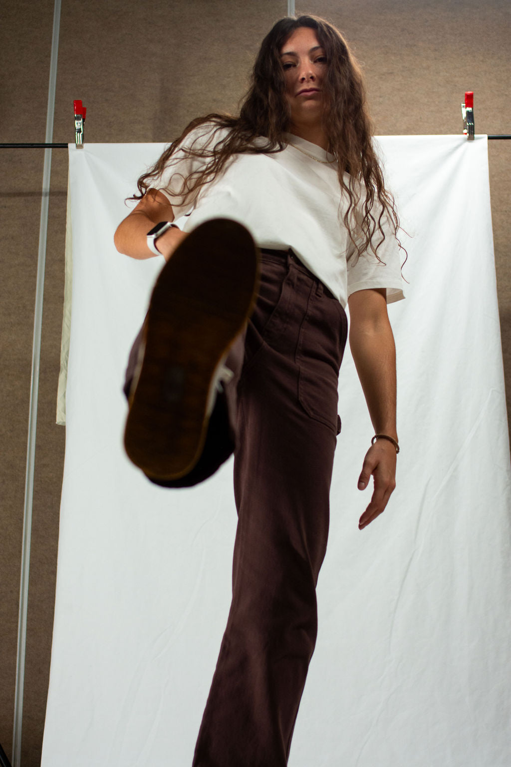 Woman wearing a white t-shirt and brown pants against a plain background