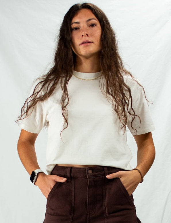 Woman wearing a white t-shirt and brown pants against a plain background