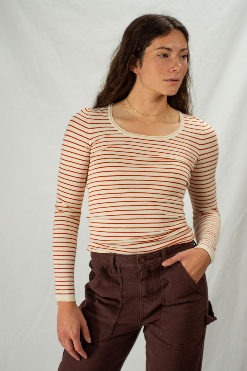 Woman wearing a rust colored striped long-sleeve top and brown pants against a plain background