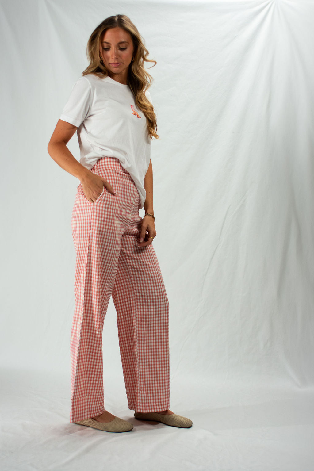 Woman wearing pink and white gingham wide leg pants with hand in pocket.
