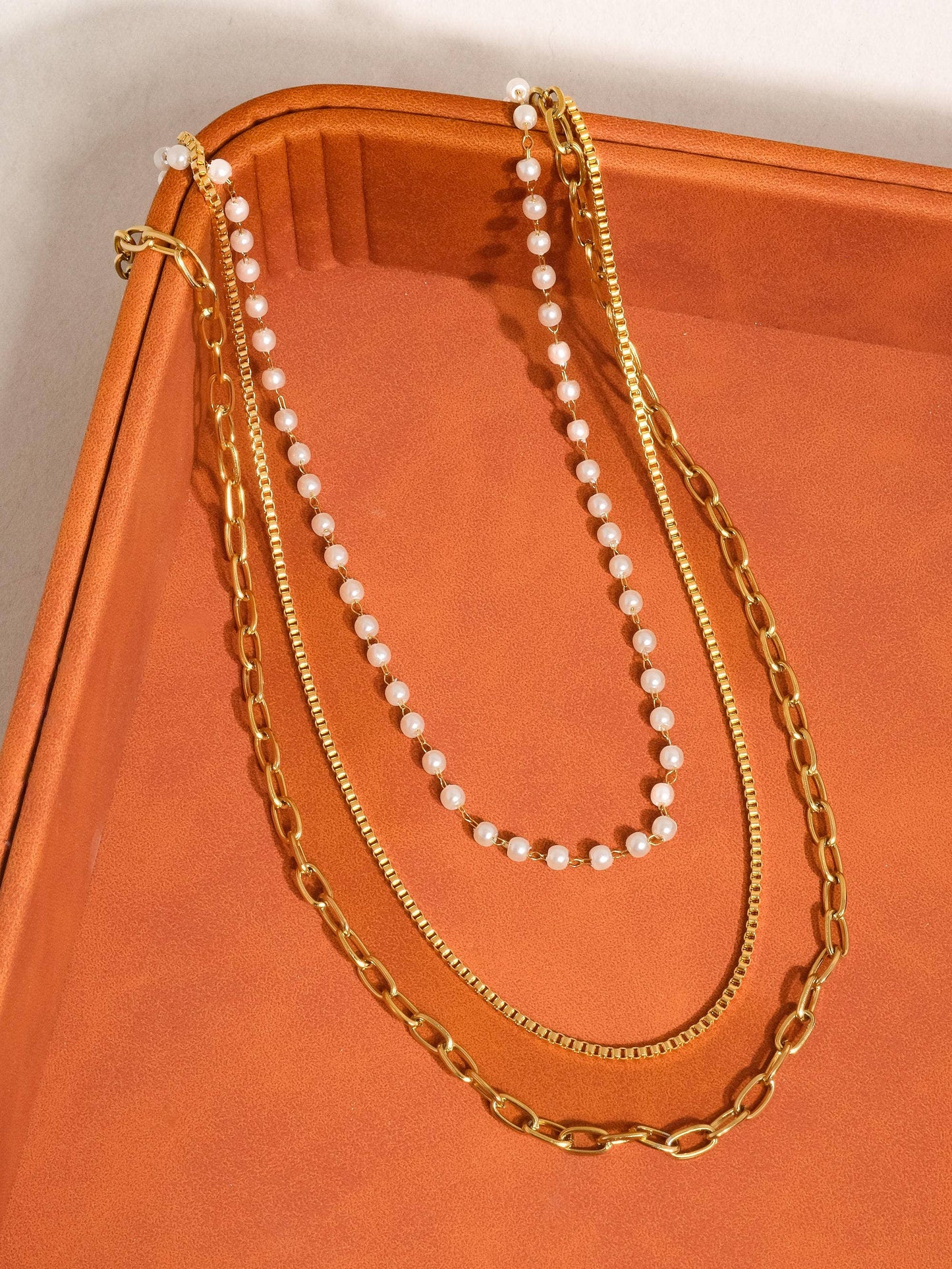 Two gold necklaces and a pearl necklace on an orange surface