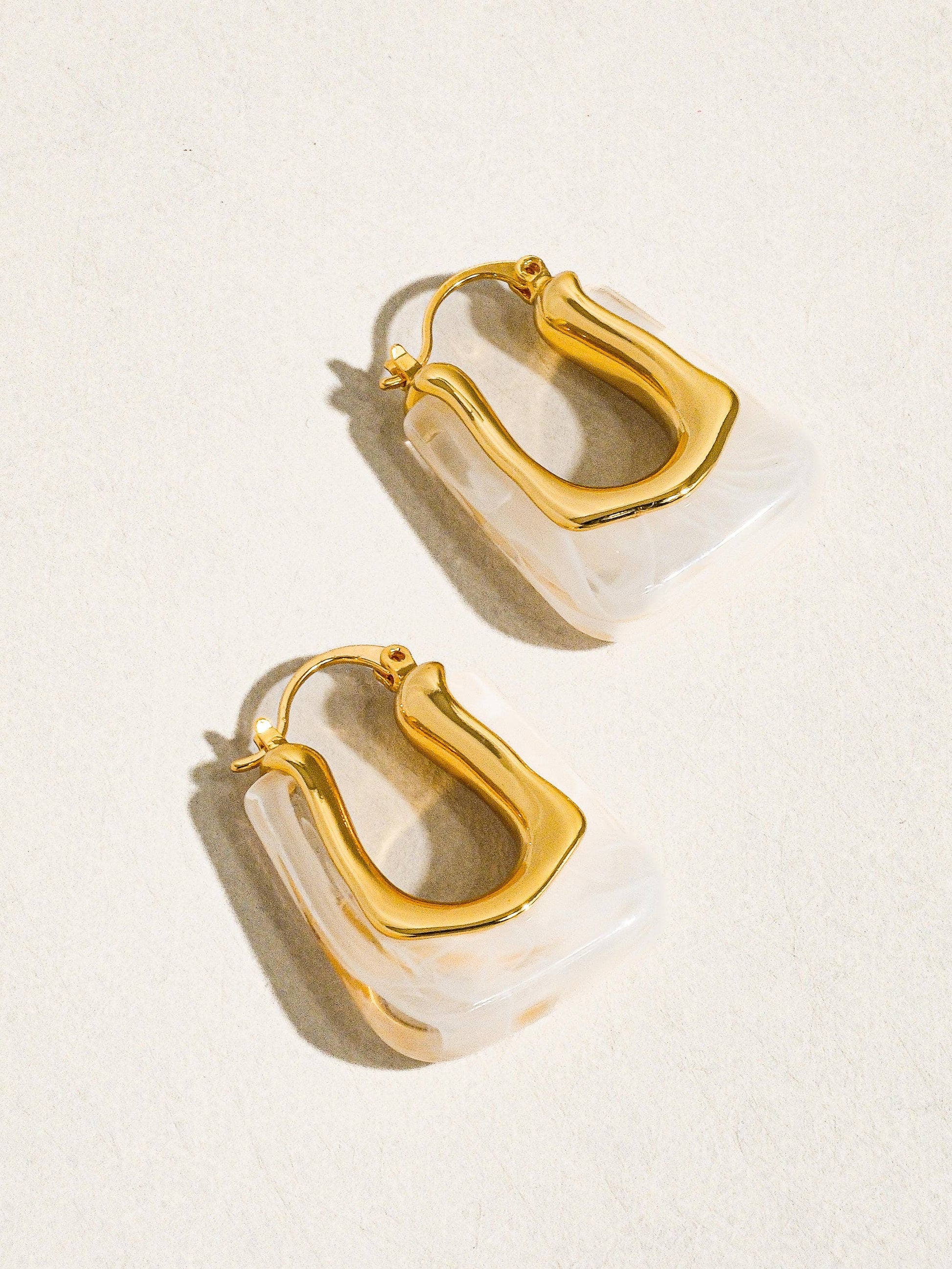 Gold hoop earrings with clear acrylic accents on a light background