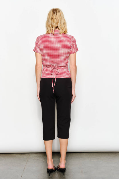 Person wearing a red checkered shirt and black pants against a white background, view from behind, the top features a tie back