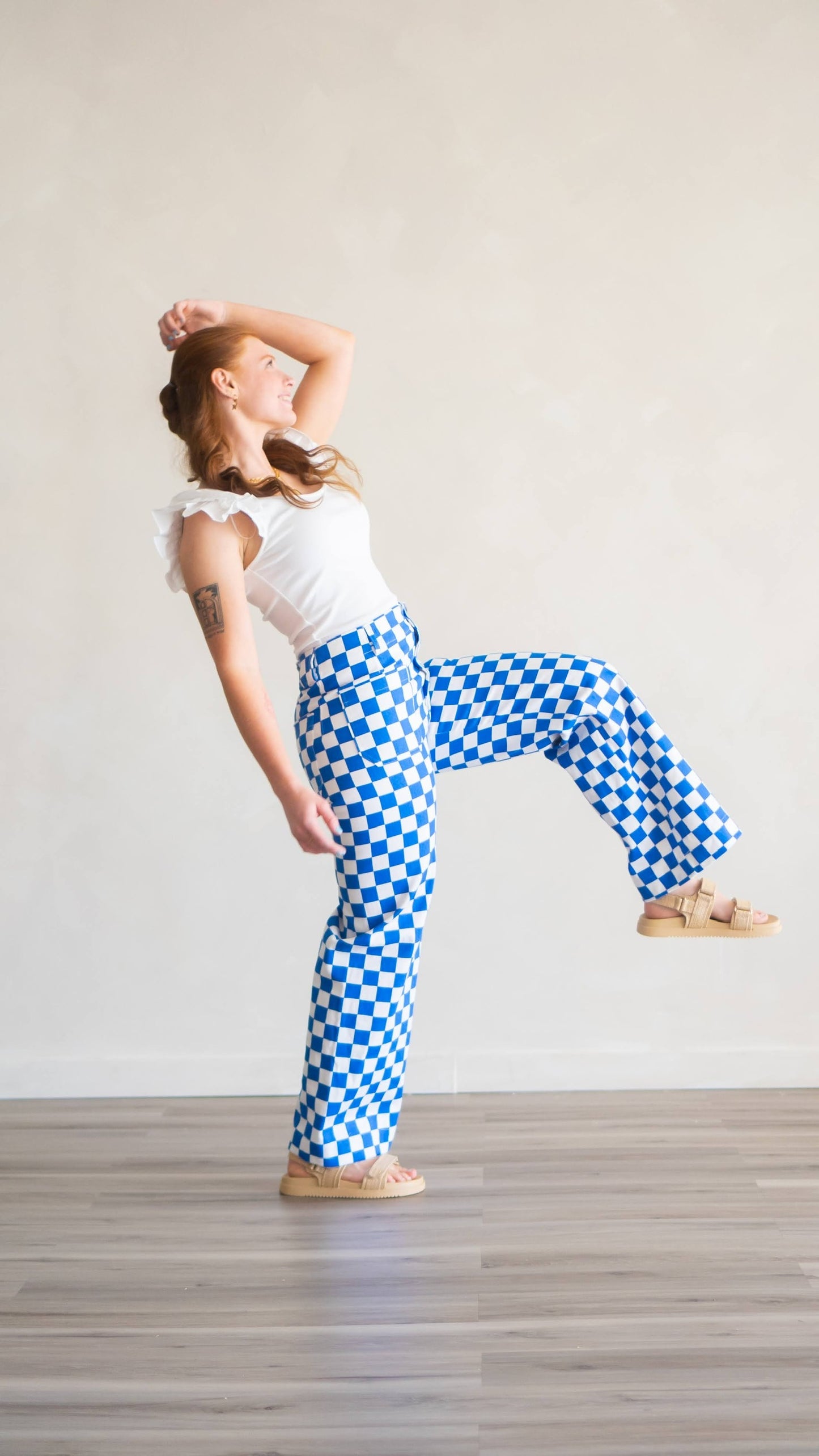 Woman leaning backward while wearing white cotton flutter sleeve top, and blue and white square denim checkered pants.