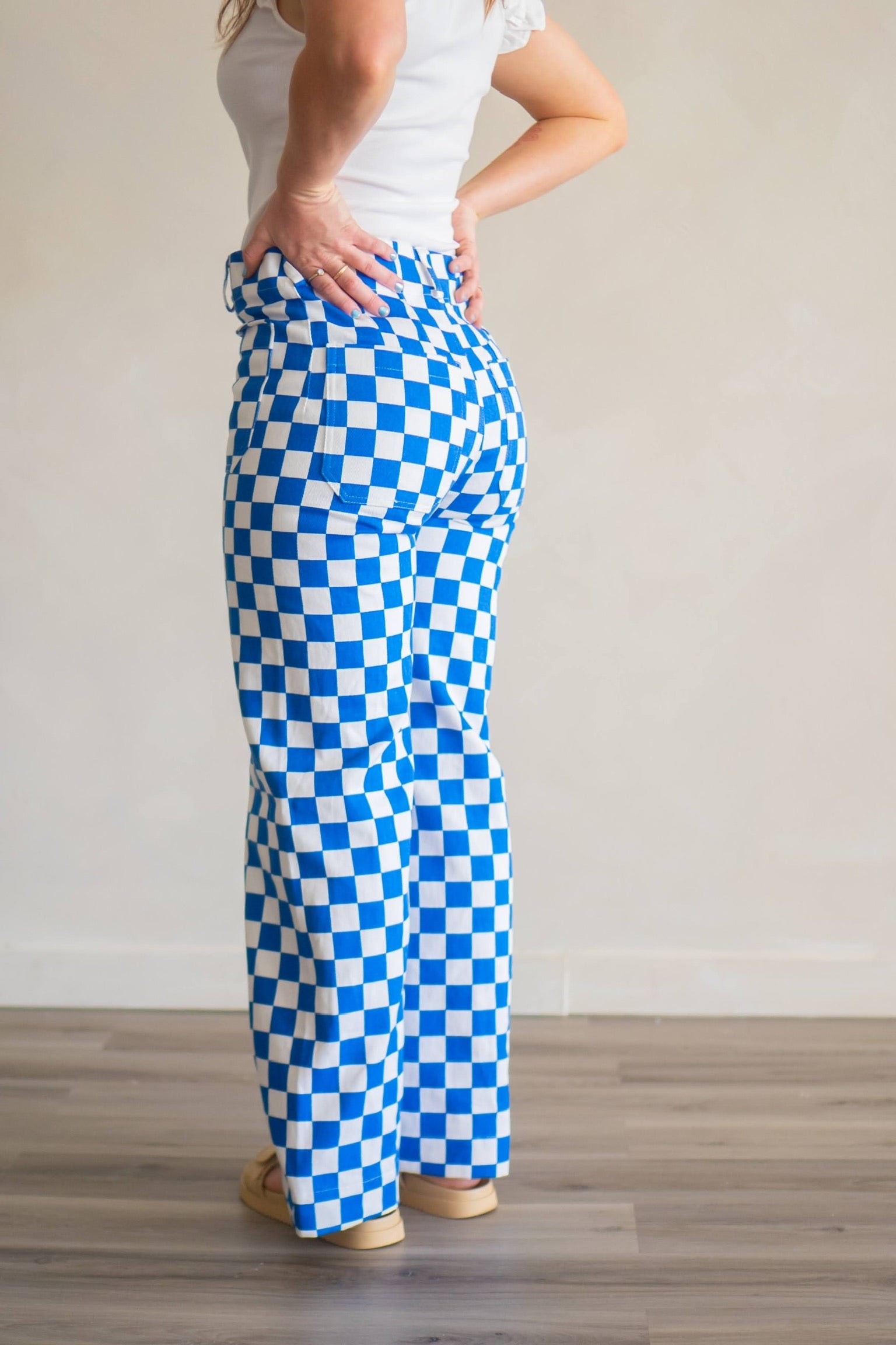 Woman with hands on hips, facing away from camera, while wearing statement pants in blue and white checkered print.