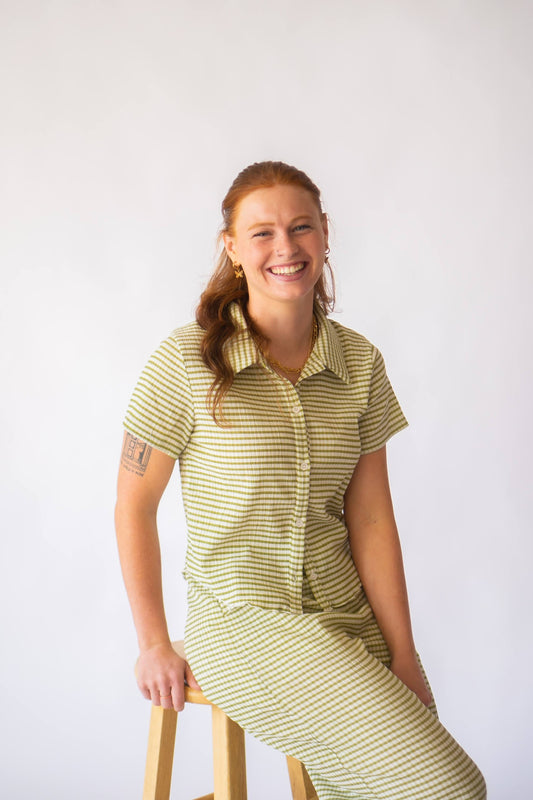 Woman wearing a green and white striped loungewear set sitting on a stool against a plain background