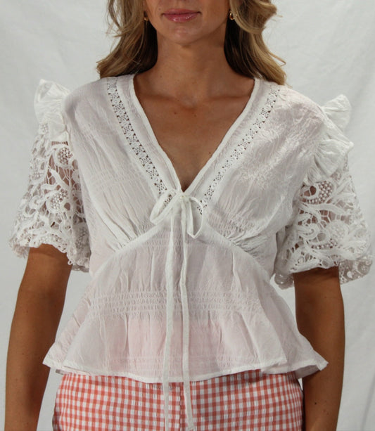 Woman wearing a white lace top with checkered pants on a plain background