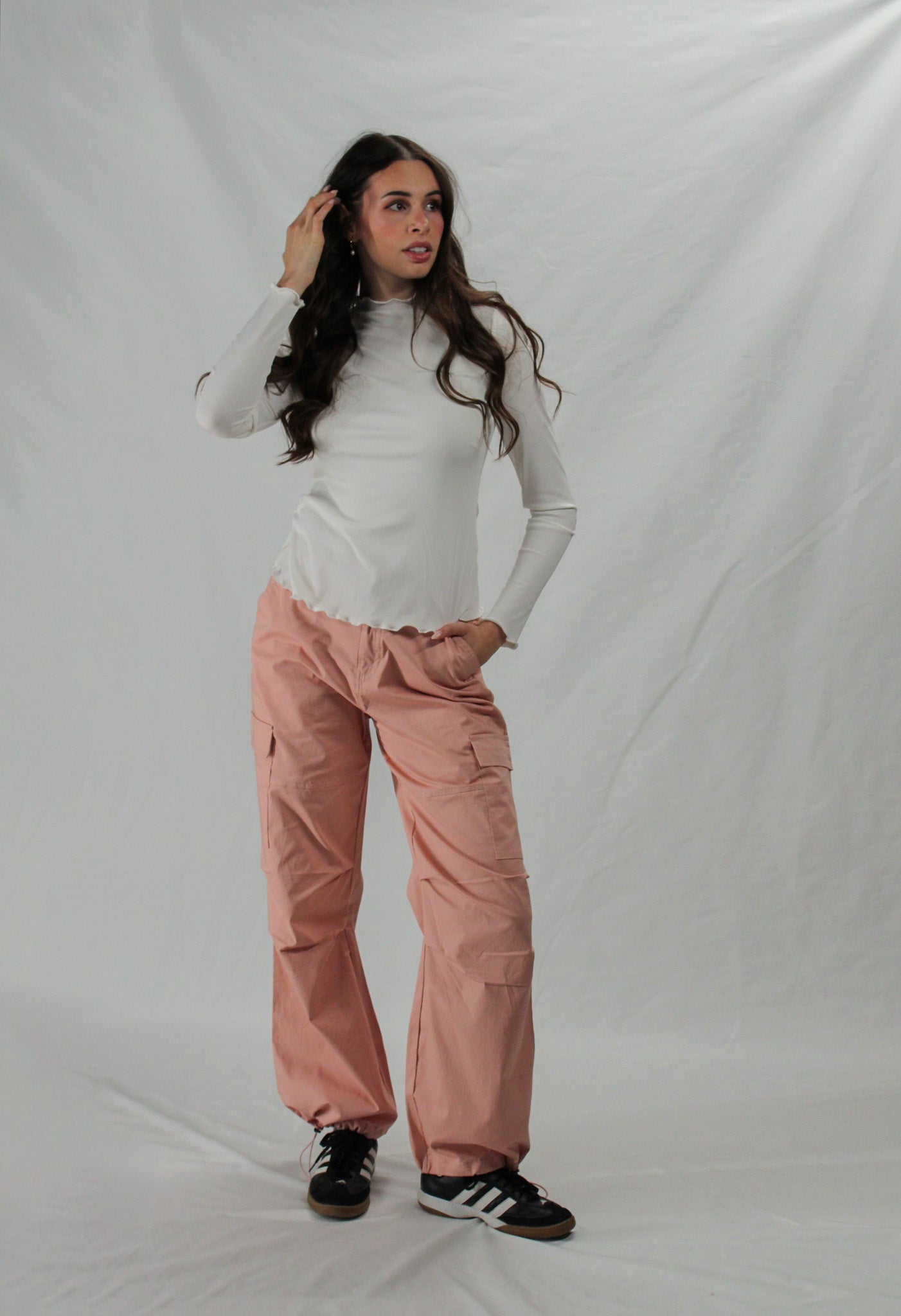 Woman wearing a white long-sleeve top and pink cargo pants against a plain background.