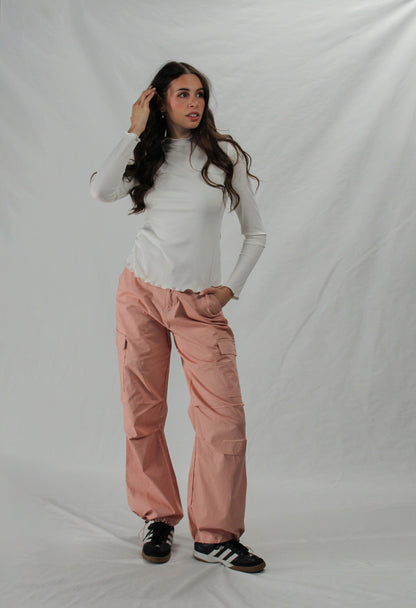 Woman wearing a white long-sleeve top and pink cargo pants against a plain background.