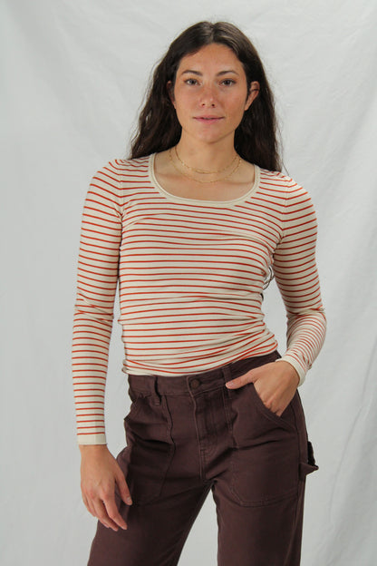 Woman wearing a cream & red striped long-sleeve top and brown pants against a plain background