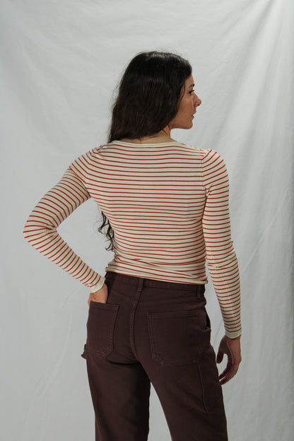 Woman wearing a cream & rust striped long-sleeve top and brown pants against a white background