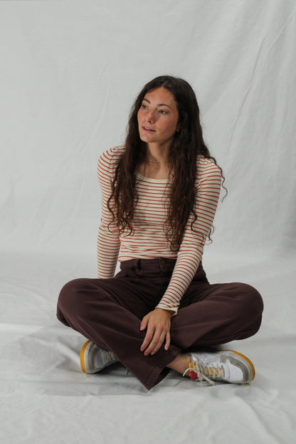 Woman sitting cross-legged on a white background wearing a striped shirt and brown pants.