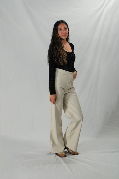 Woman wearing cream leather pants with cowboy boots and a black scoop neck top