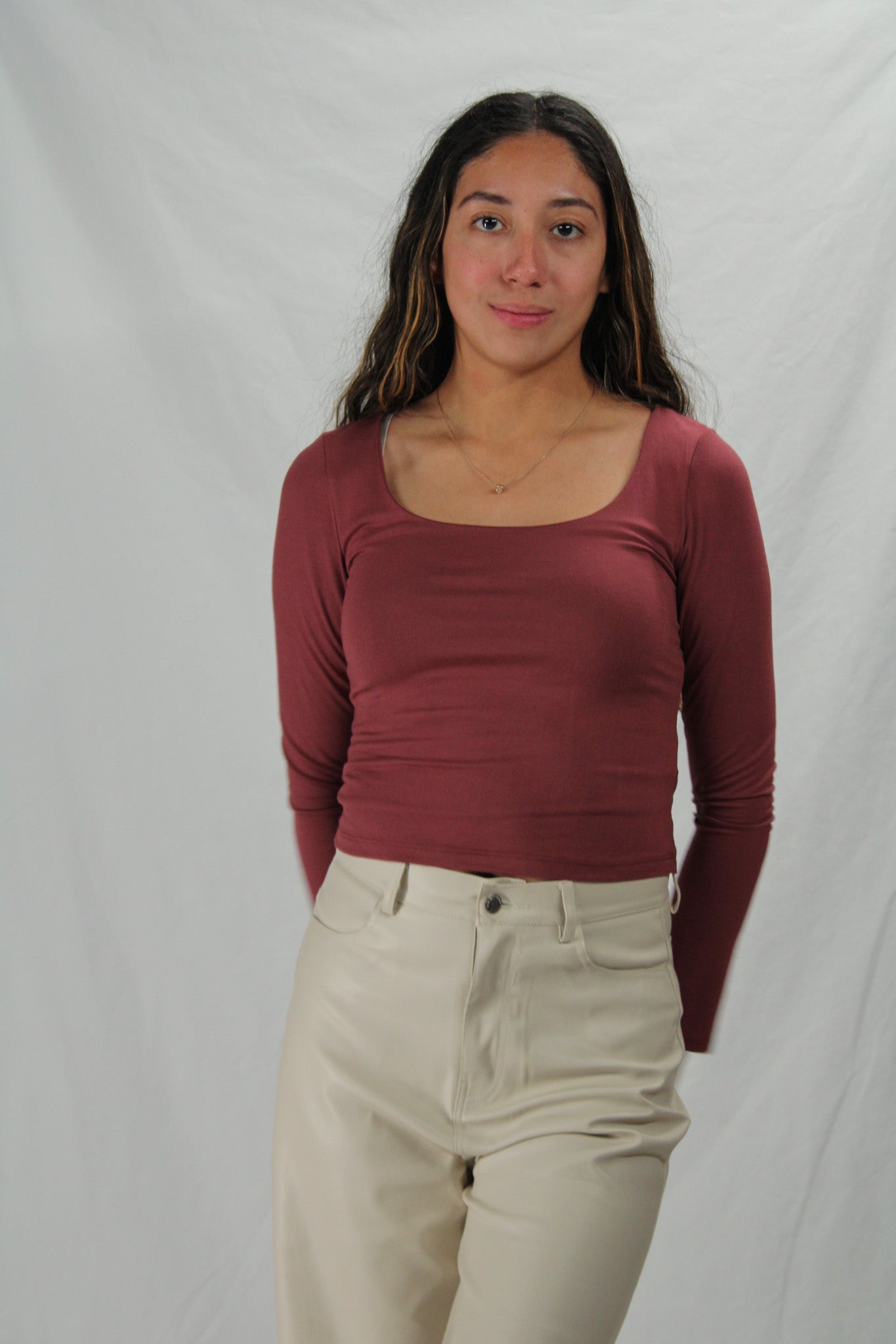 Woman wearing a maroon long-sleeve top and beige pants against a plain background