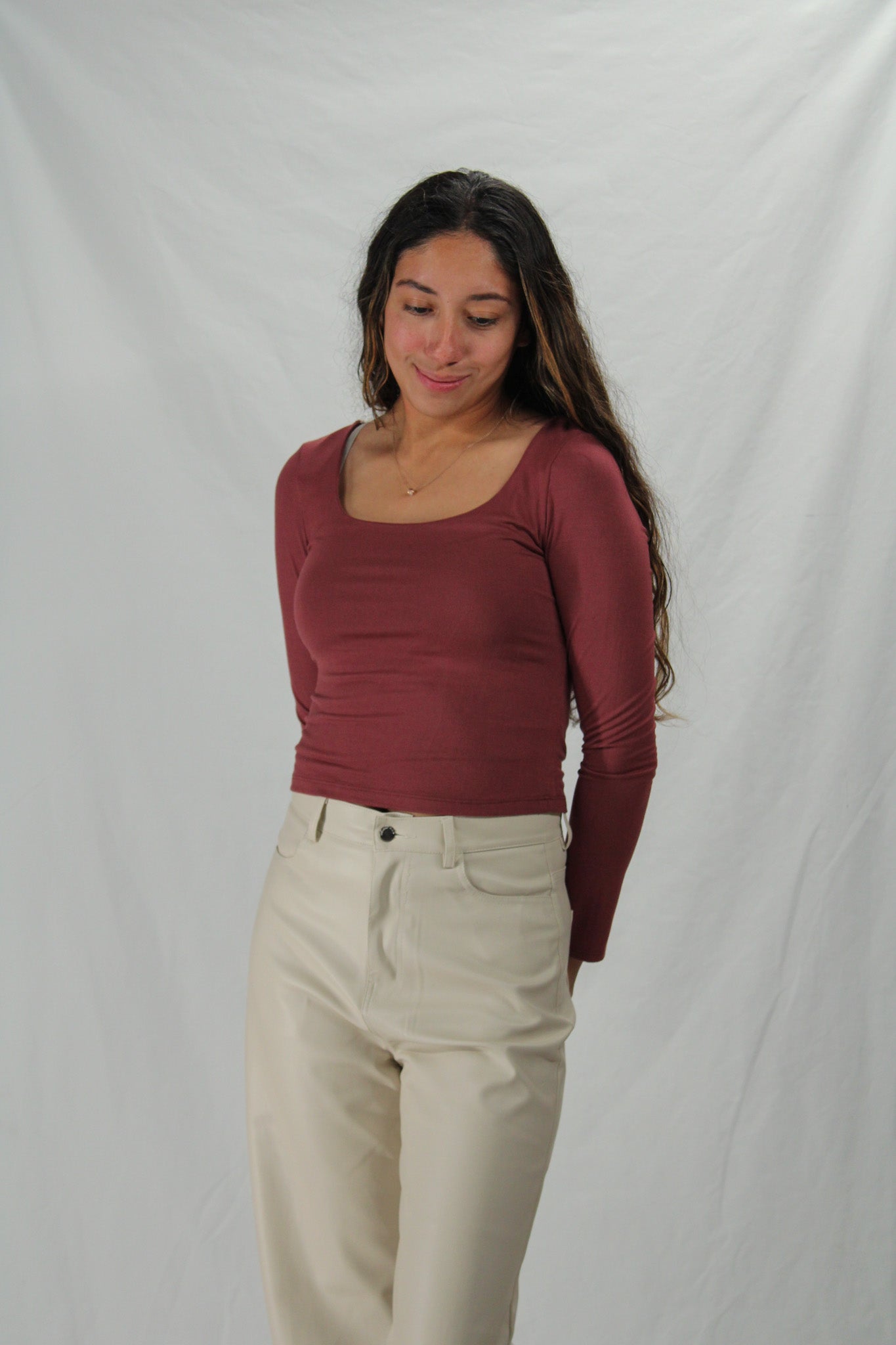 Woman wearing a burgundy long-sleeve top and beige pants against a plain background