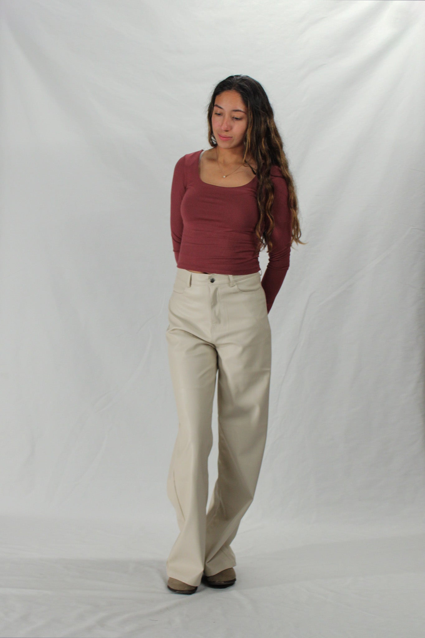 Woman wearing a maroon long-sleeve top and beige pants against a white background