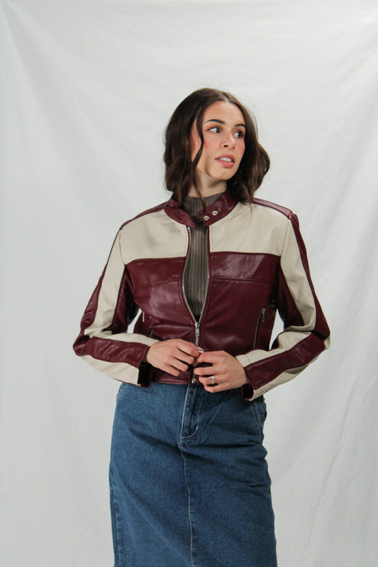 Woman wearing a maroon and beige leather jacket with blue jeans on a white background