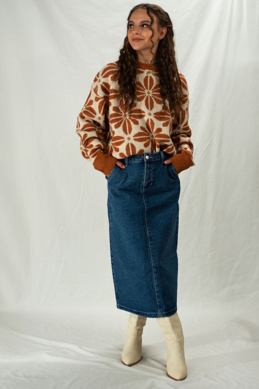 Woman wearing a patterned sweater and blue denim skirt against a white background