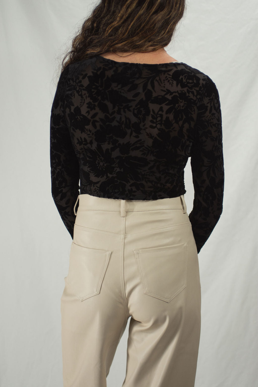 Woman wearing a black bodysuit with floral velvet accents and long sleeves, slightly sheer.