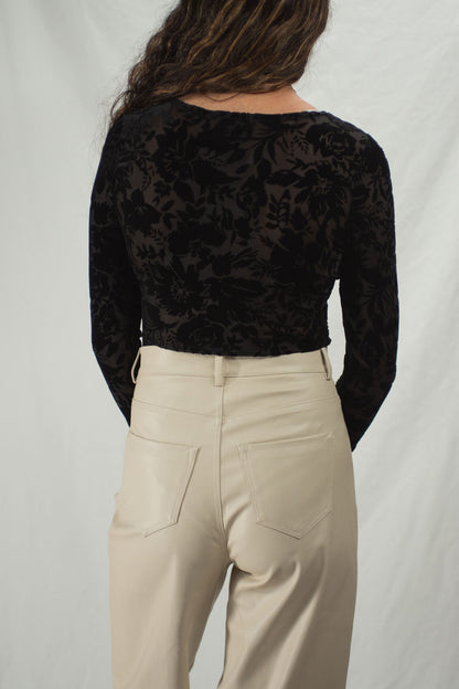 Woman wearing a black bodysuit with floral velvet accents and long sleeves, slightly sheer.