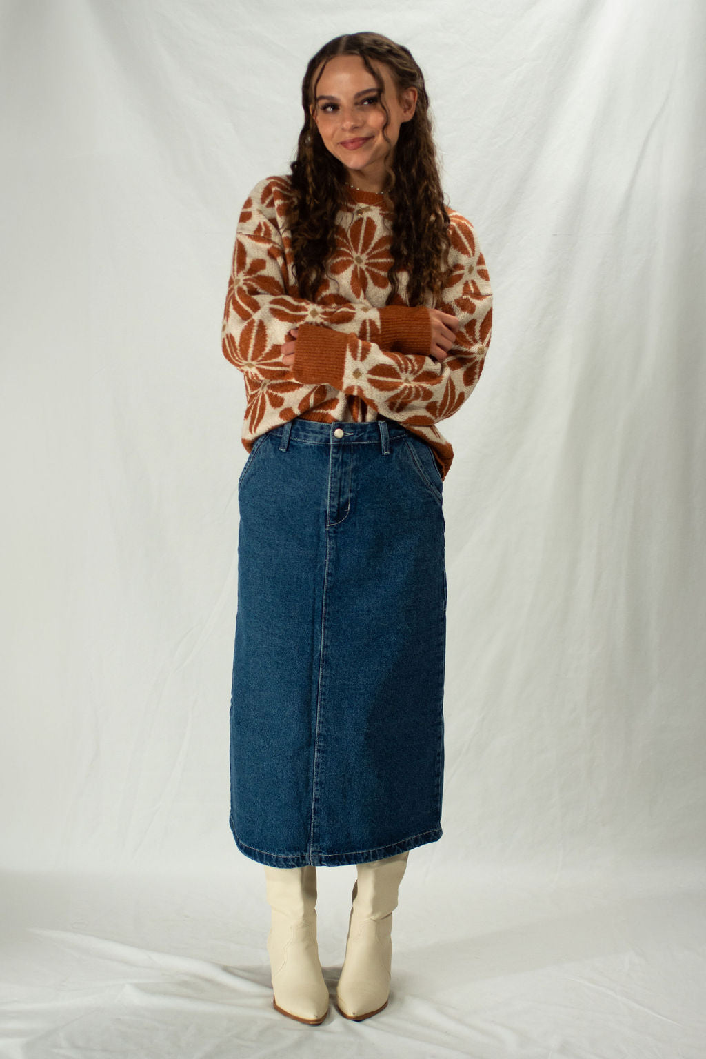 Person wearing a patterned sweater and denim skirt against a white background