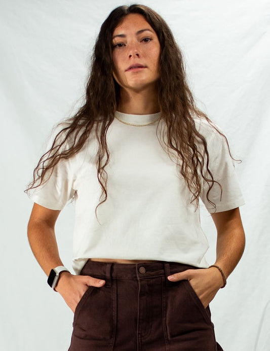 Woman wearing a white t-shirt and brown pants against a plain background