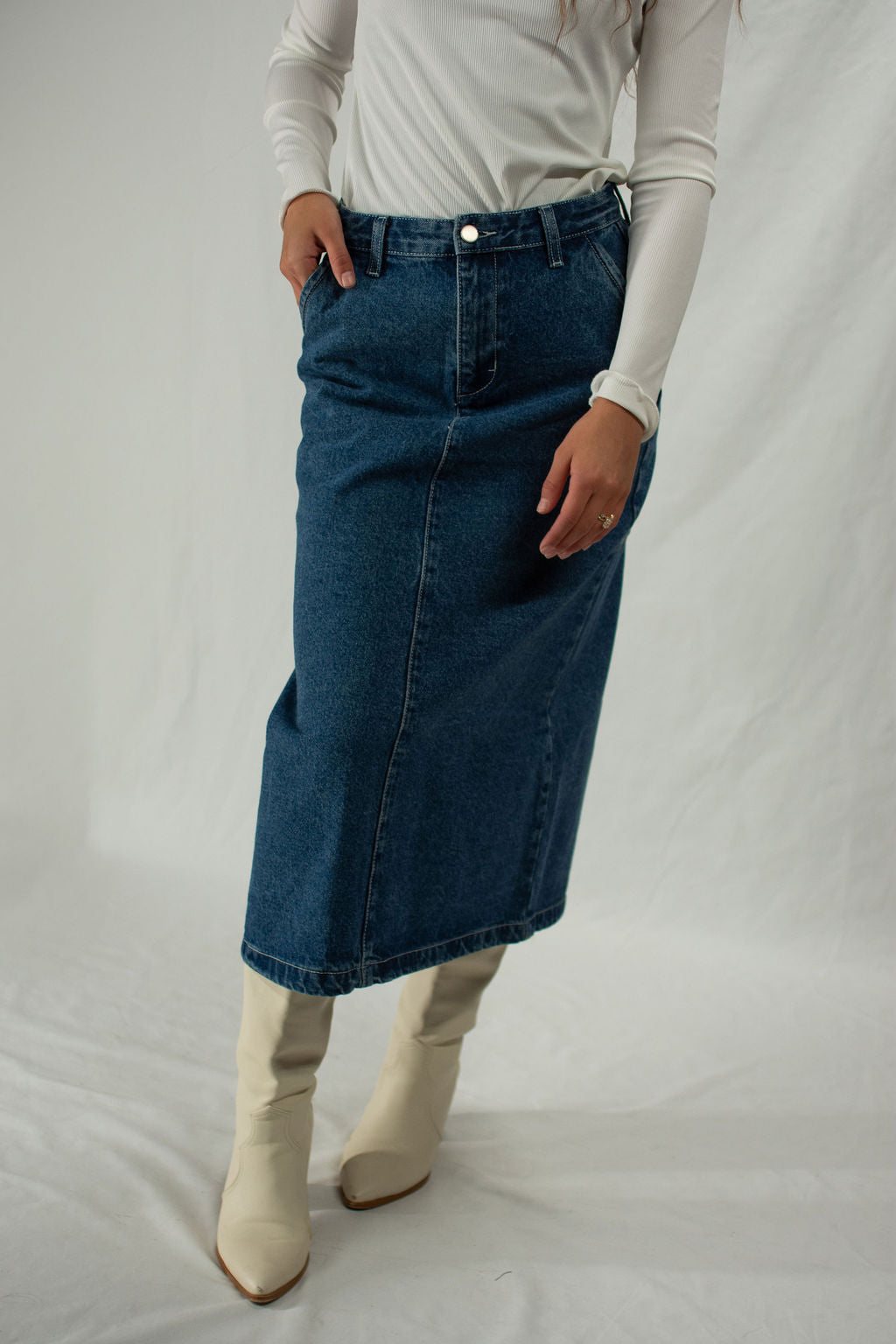 Person wearing a blue denim skirt and white boots on a plain background