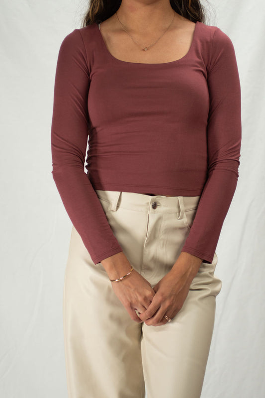 Person wearing a mauve long-sleeve top and beige pants on a white background