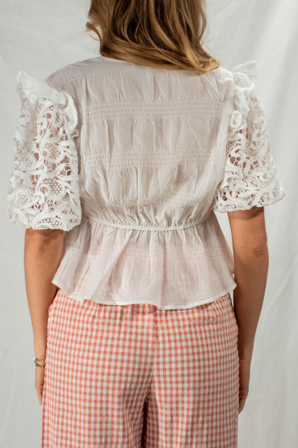 Woman wearing a light blouse with lace sleeves and pink checkered pants on a plain background
