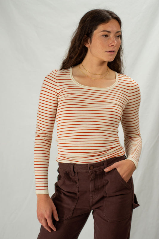 Woman wearing a rust colored striped long-sleeve top and brown pants against a plain background