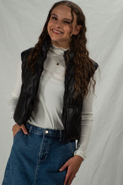 Woman wearing black zip up leather puffer vest with white mock neck