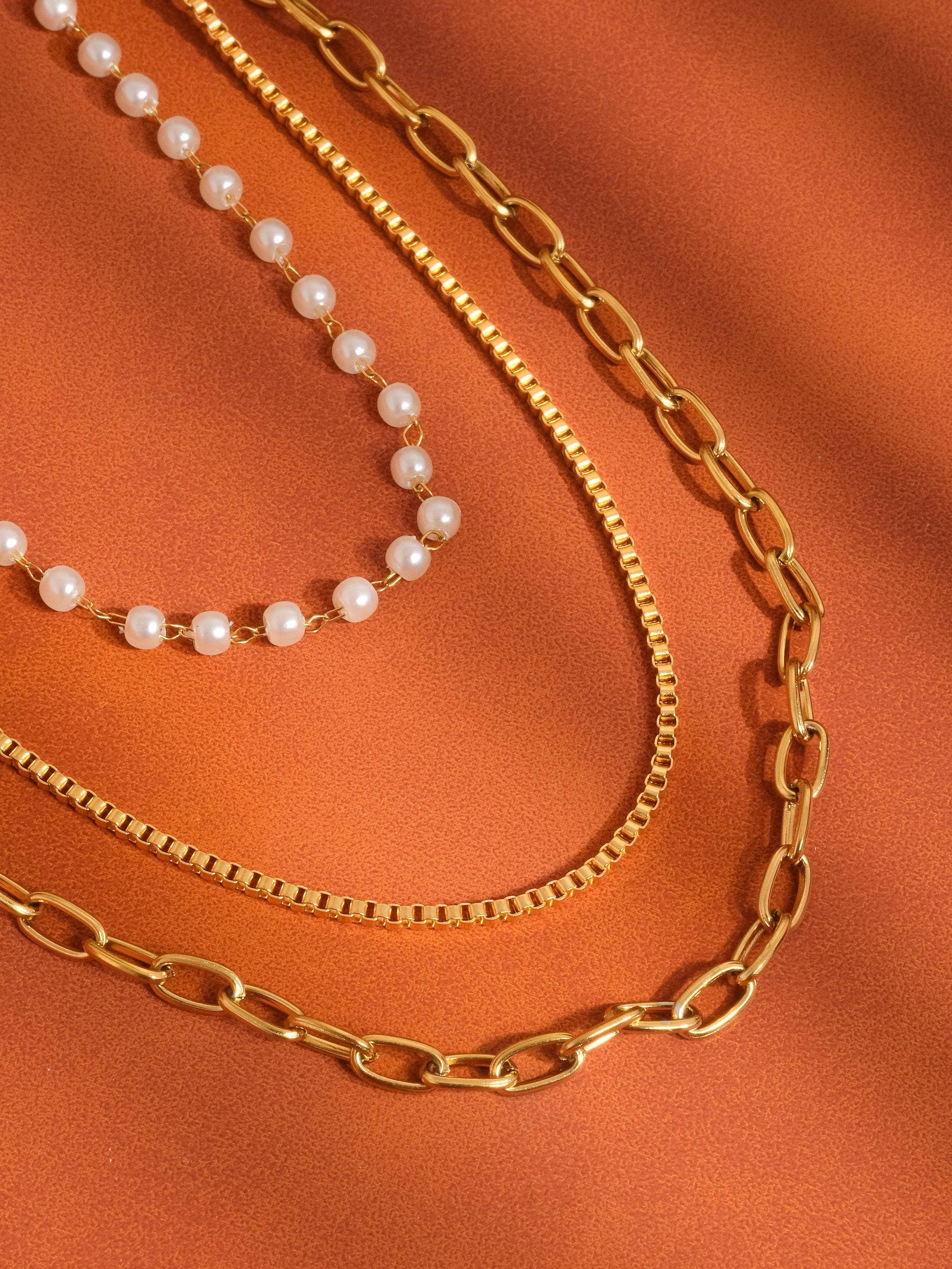 Two gold chains and a pearl necklace on an orange fabric background