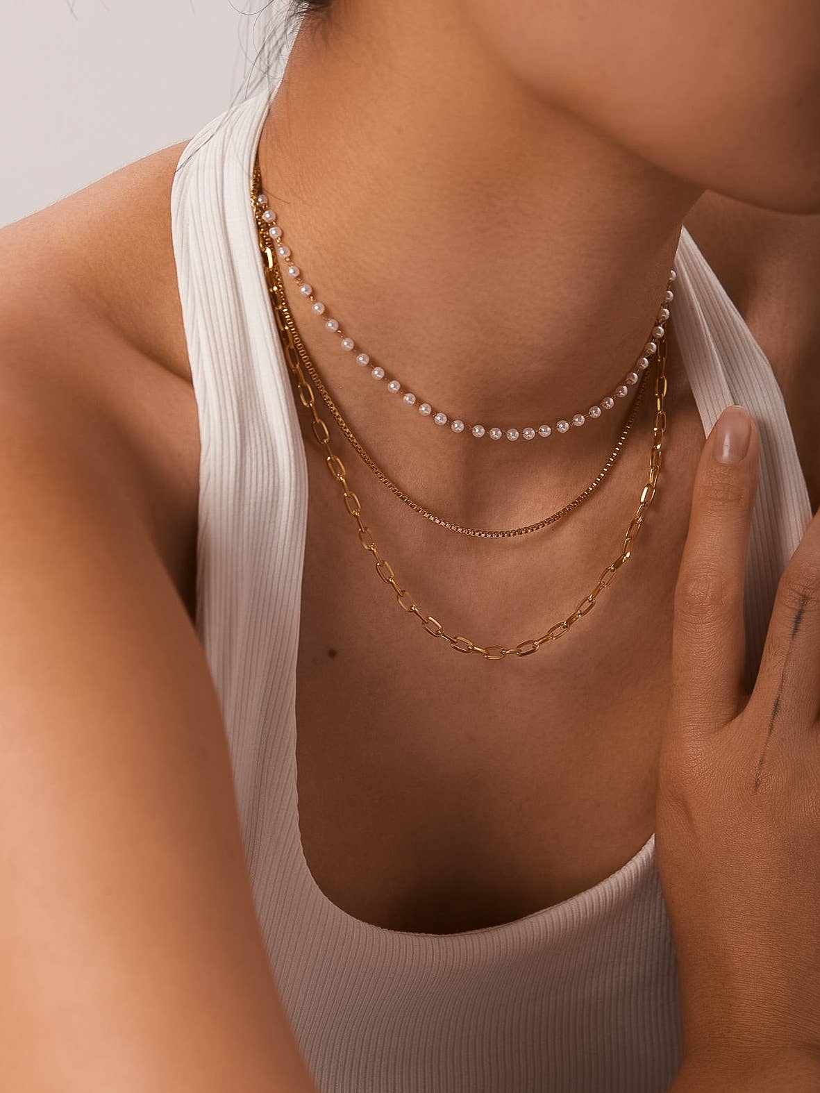 Close-up of a person wearing multiple gold necklaces and a pearl necklace