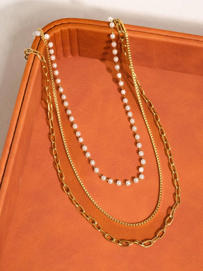 Two gold necklaces and a pearl necklace on an orange surface