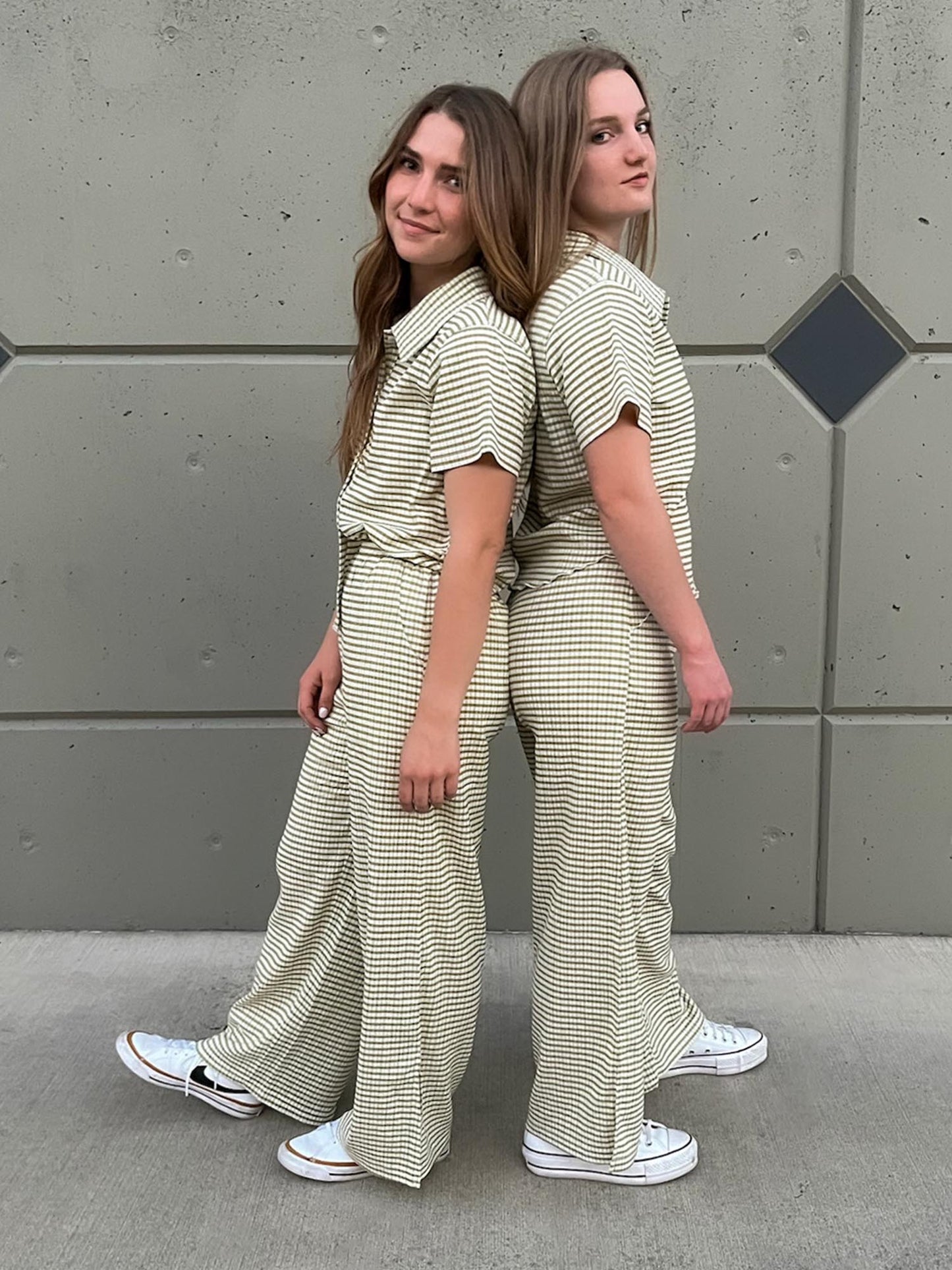 Two girls standing back to back wearing a green striped set with button up shirt and split hem pants