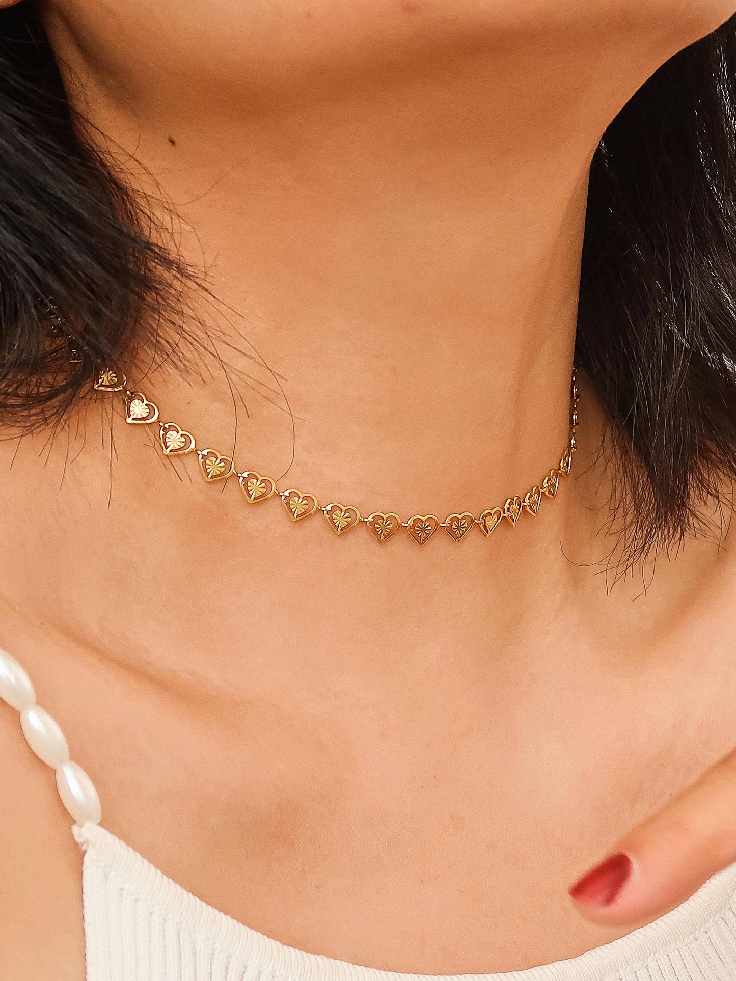 Gold heart-shaped choker necklace on a person wearing a white top.