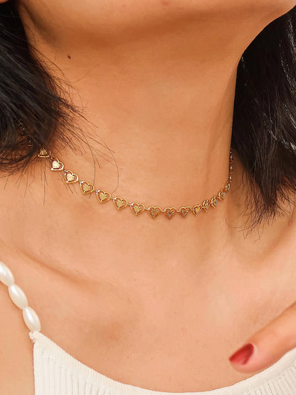 Gold heart-shaped choker necklace on a person wearing a white top.