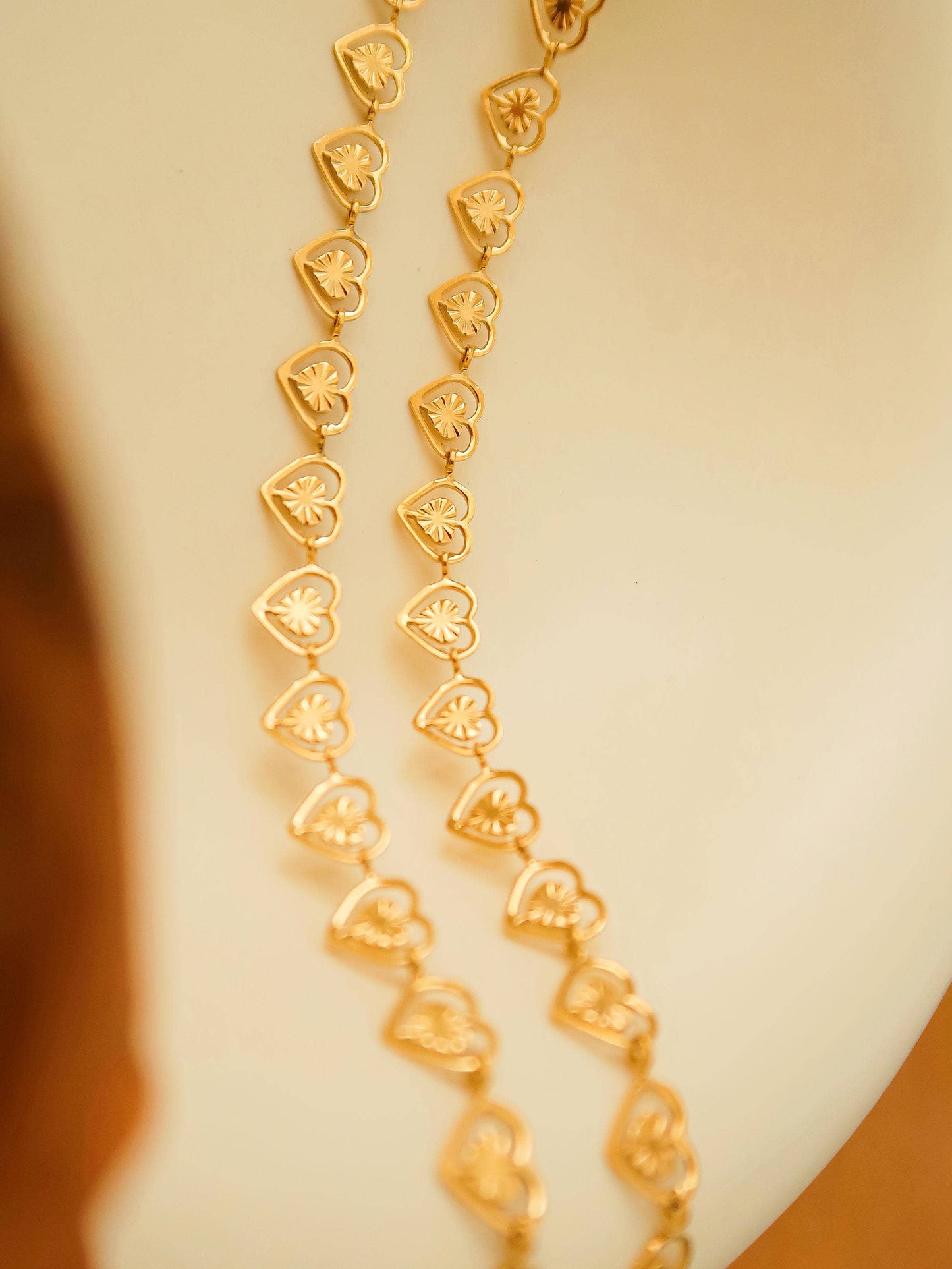 Gold necklace with heart-shaped links on a neutral background
