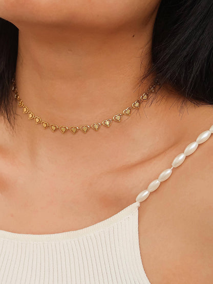 Gold heart-shaped necklace worn by a person with a white top